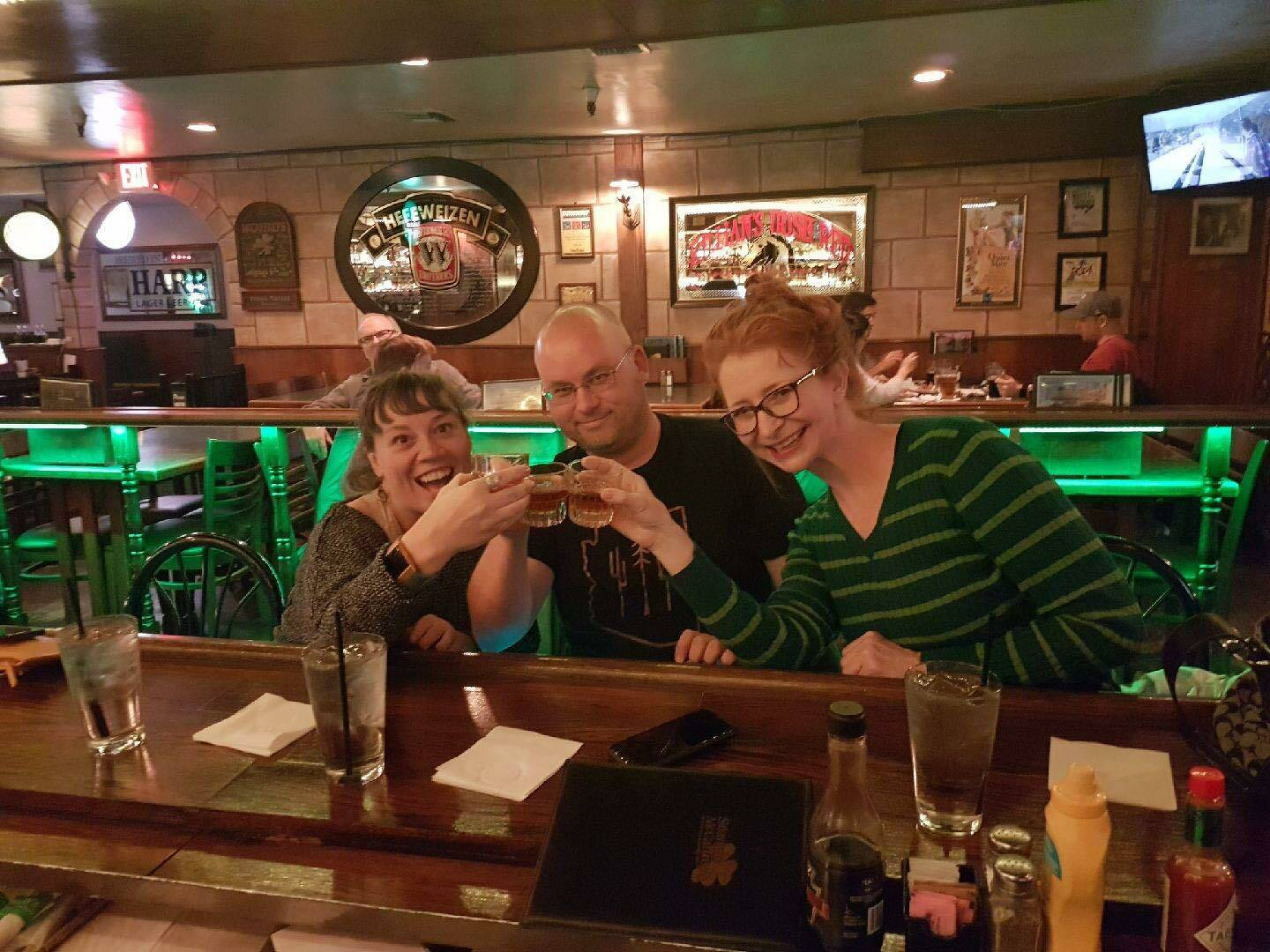 Auto-generated description: Three people are sitting at a bar, raising their drinks in a toast.