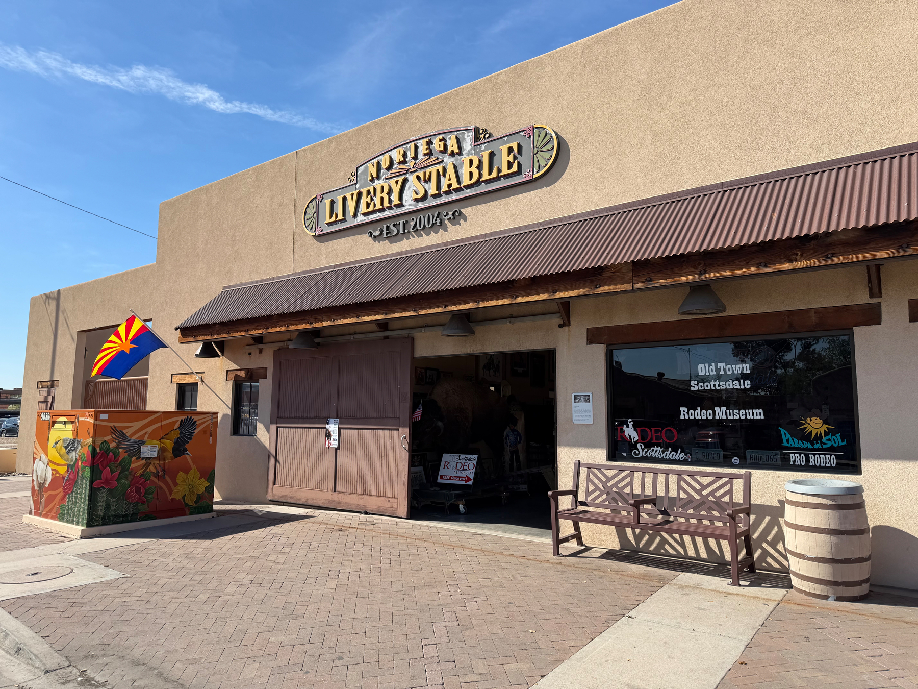 A rustic building houses the Old Town Scottsdale Rodeo Museum, featuring a wooden exterior, a Livery Stable sign, and a colorful mural and artistic Arizona flag at the entrance.